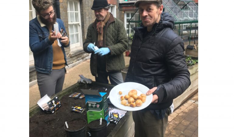 Gardeners taking a break, one holding a plate of potatoes.